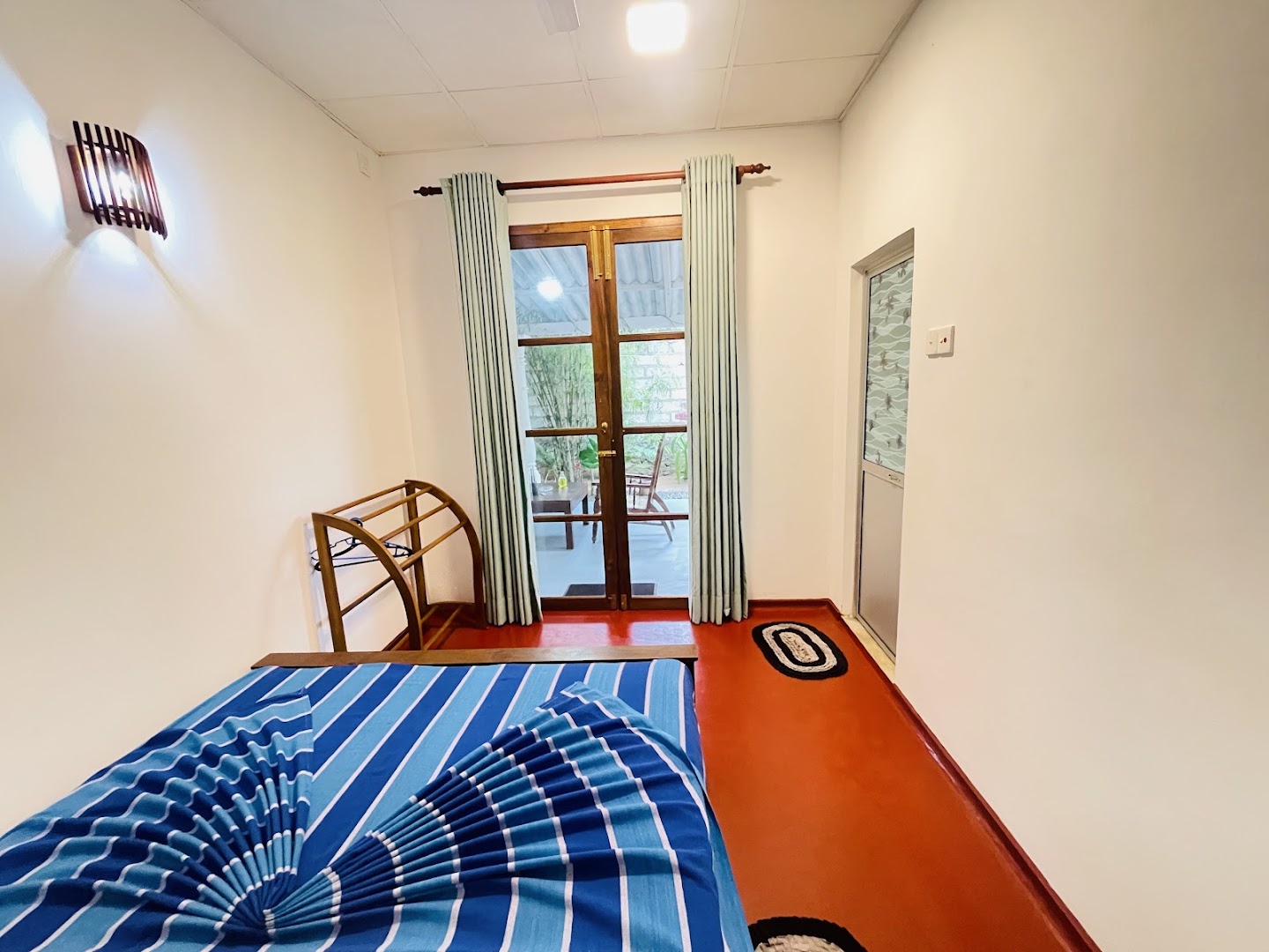 Simple guest room with white walls, timber doors, curtains, and blue bedding